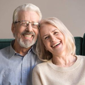 Head,Shot,Laughing,Retirees,Pretty,Couple,Sitting,On,Couch,At